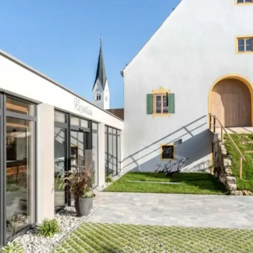 Hotel Pöltner Hof in Weilheim in Oberbayern, ein helles Gebäude mit grünem Innenhof bei tollem Wetter